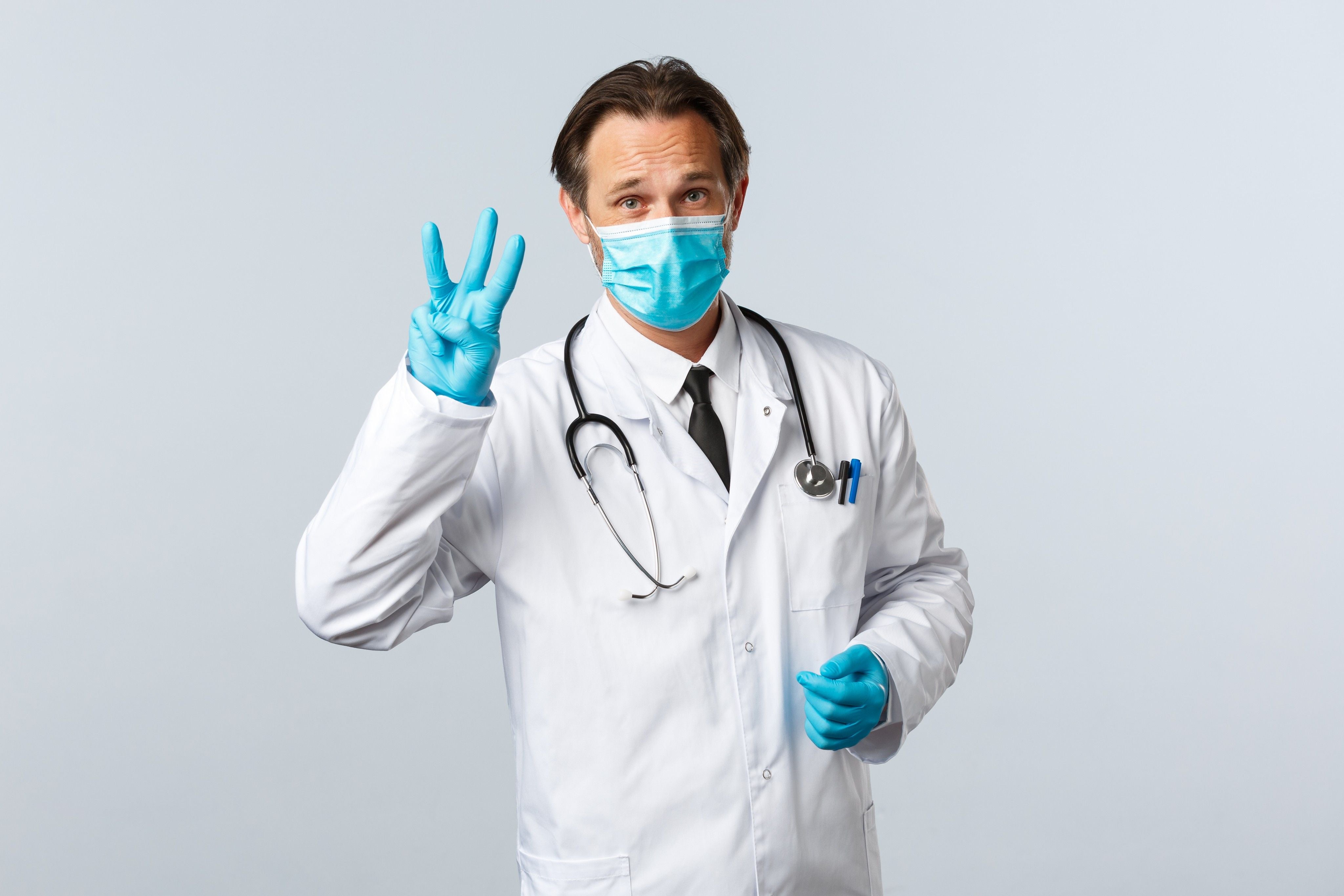 Male urologist in blue gloves and mask holding up three fingers to indicate the three prostate zones.